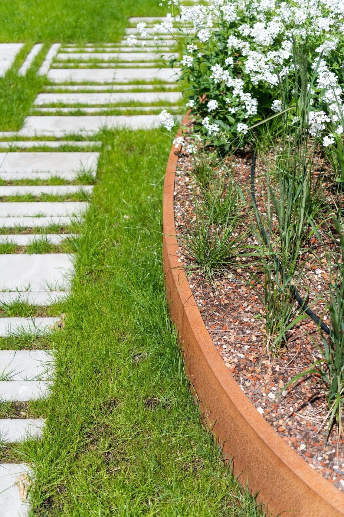 Ronde keerwand in cortenstaal om het  plantenvak af te scheiden van het gras